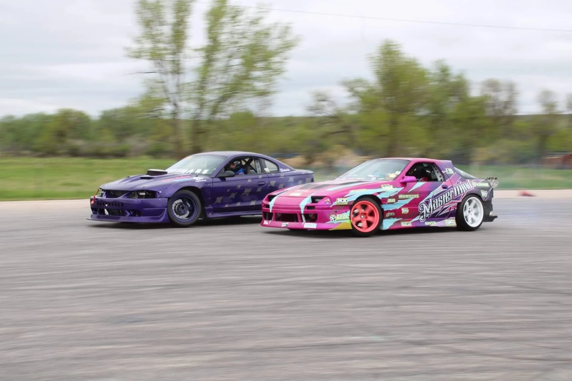 Purple Mustang and pink RX-7 drifting in tandem